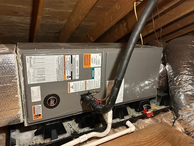 HVAC unit installed in an attic. Gray metal box with ductwork and piping. Black support structure.