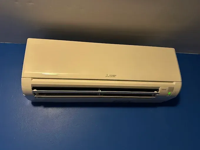 A white Mitsubishi mini-split air conditioner mounted on a blue wall.