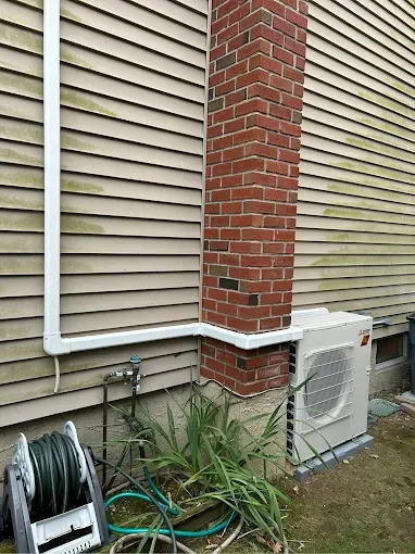Brick chimney next to a beige-sided house. An AC unit sits below, with white piping running to the house.