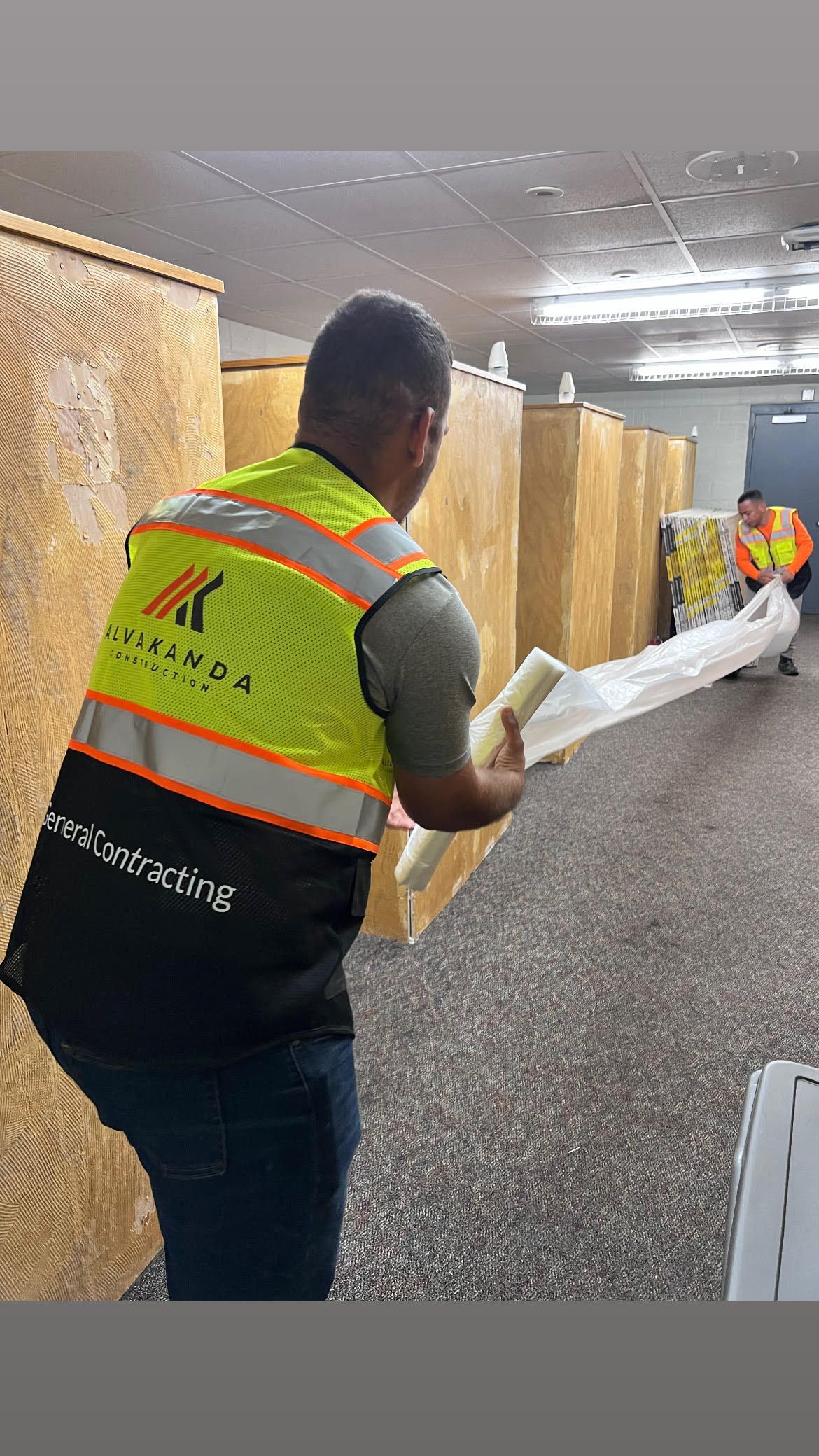 A man in a yellow vest is holding a piece of paper in a room.