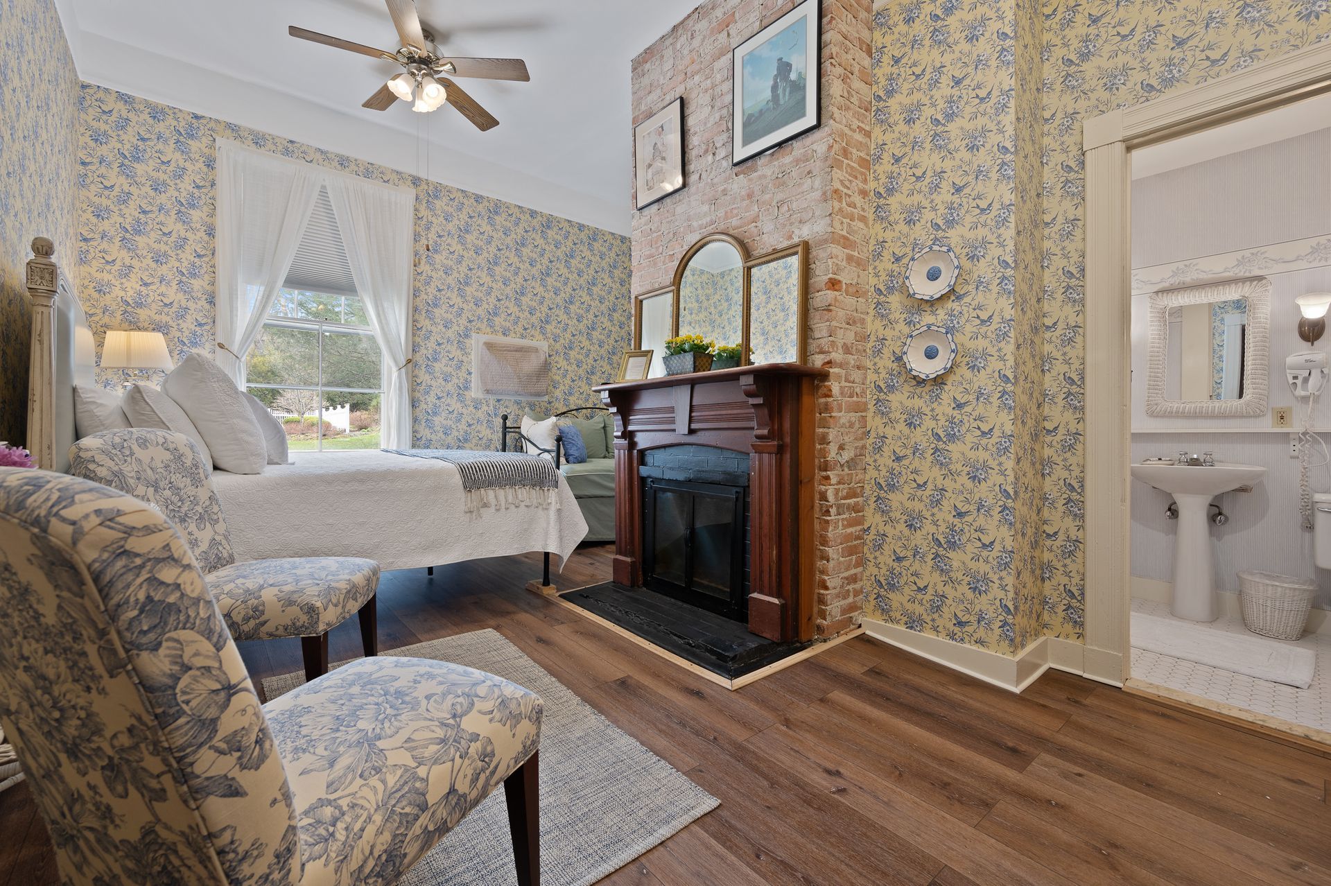 A bedroom with two beds , chairs , a fireplace and a ceiling fan.
