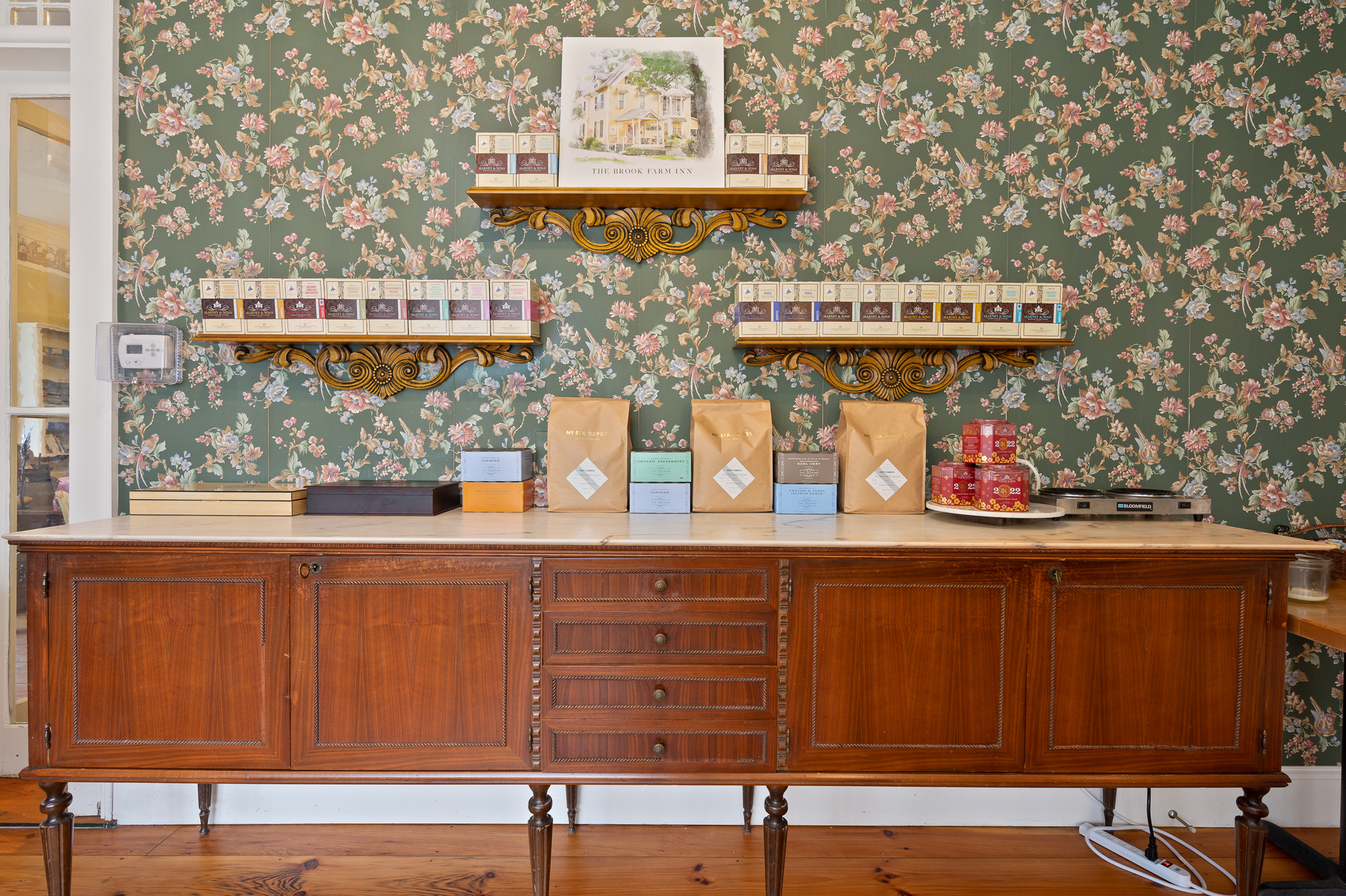 A long wooden table with boxes on it in front of a floral wallpaper.