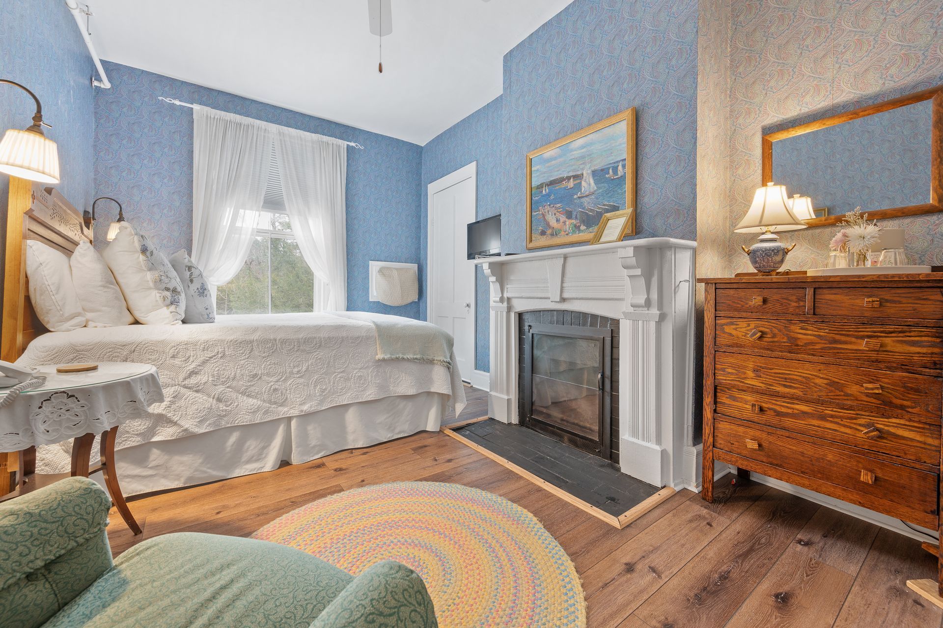 A bedroom with a bed , dresser , chair and fireplace.