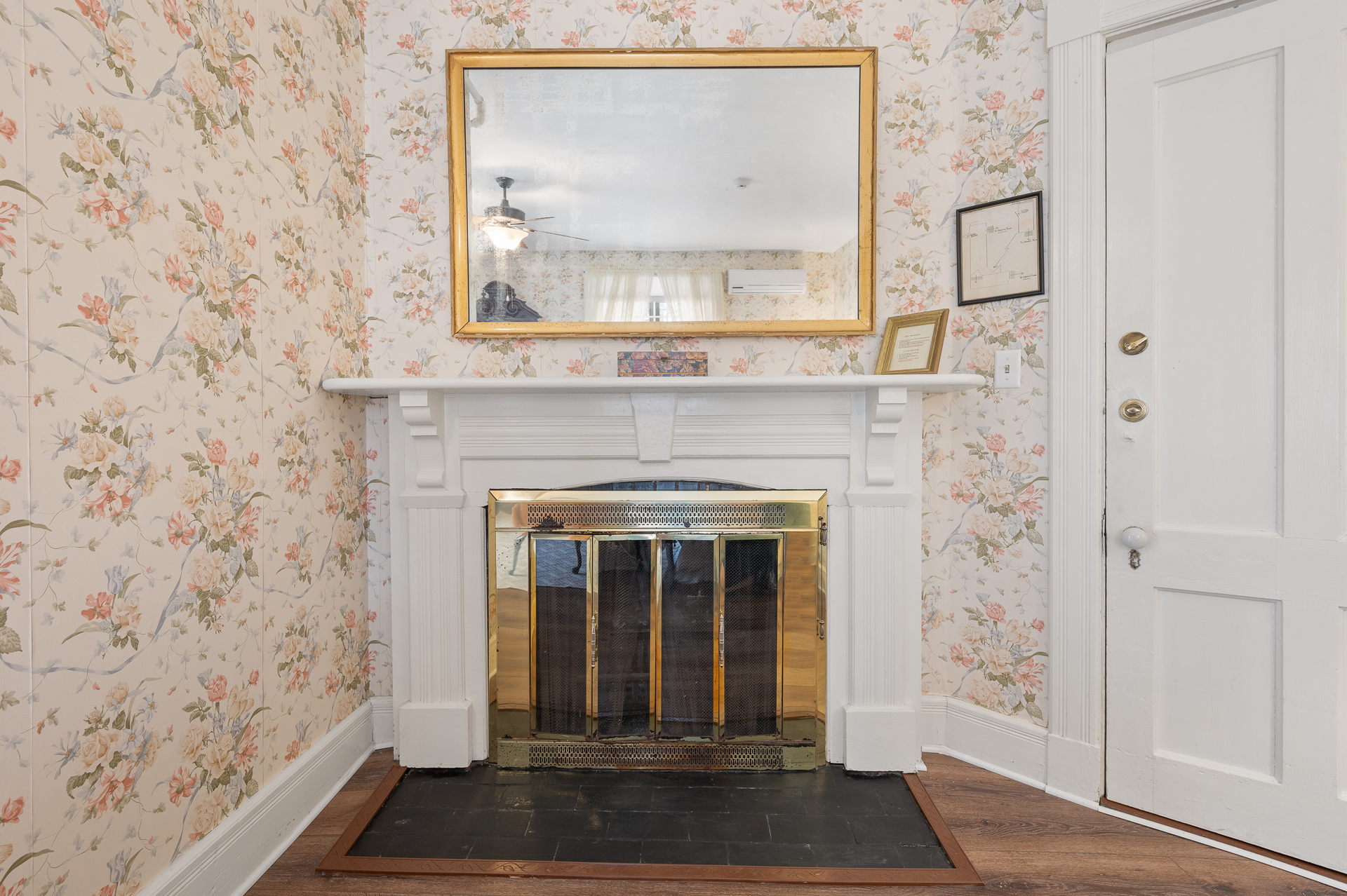 A living room with a fireplace , mirror and floral wallpaper.