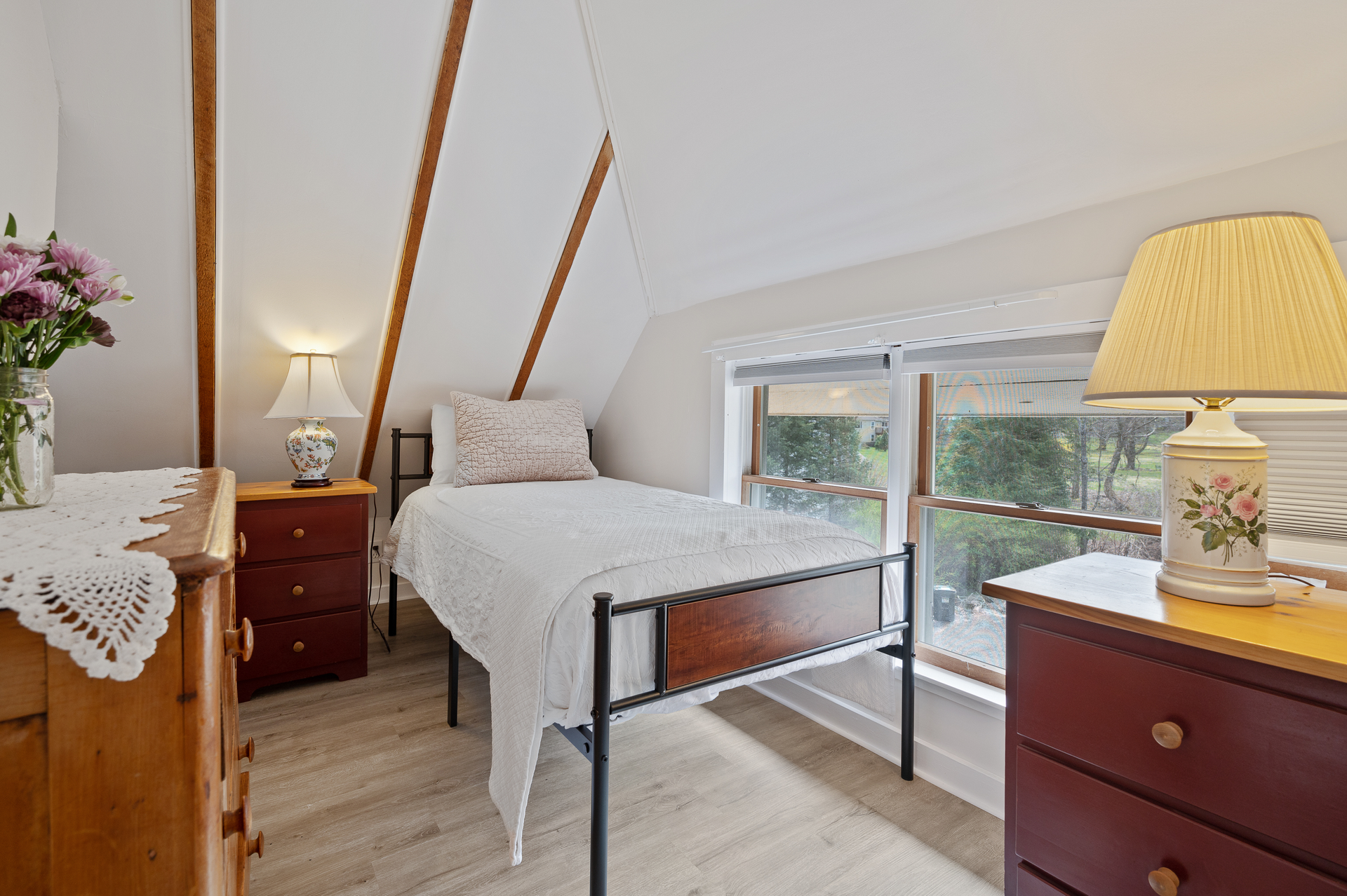 A bedroom with a bed , dresser , lamp and window.