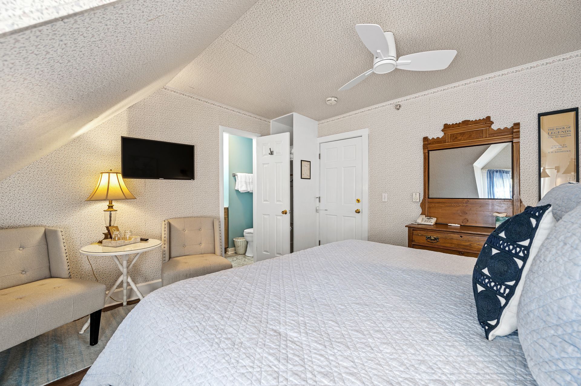 A bedroom with a bed , chairs , a table and a ceiling fan.