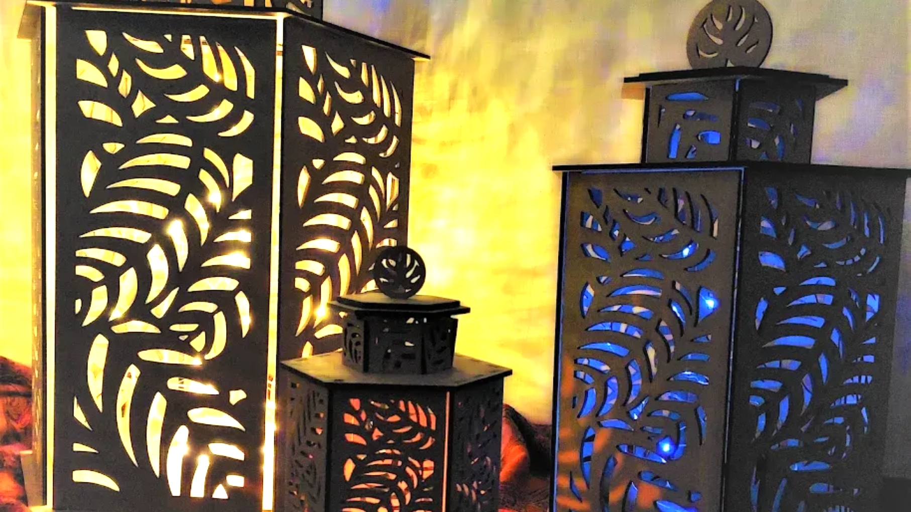 Three black metal lanterns with leaf cutouts; lit from within, casting leaf shadows.