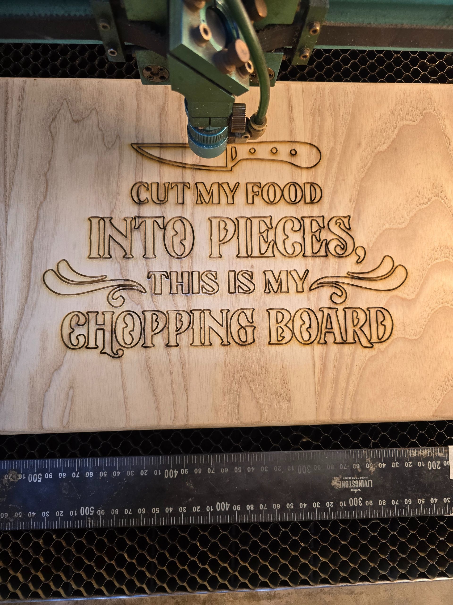 Laser engraver burning text and a knife image onto a wooden cutting board.