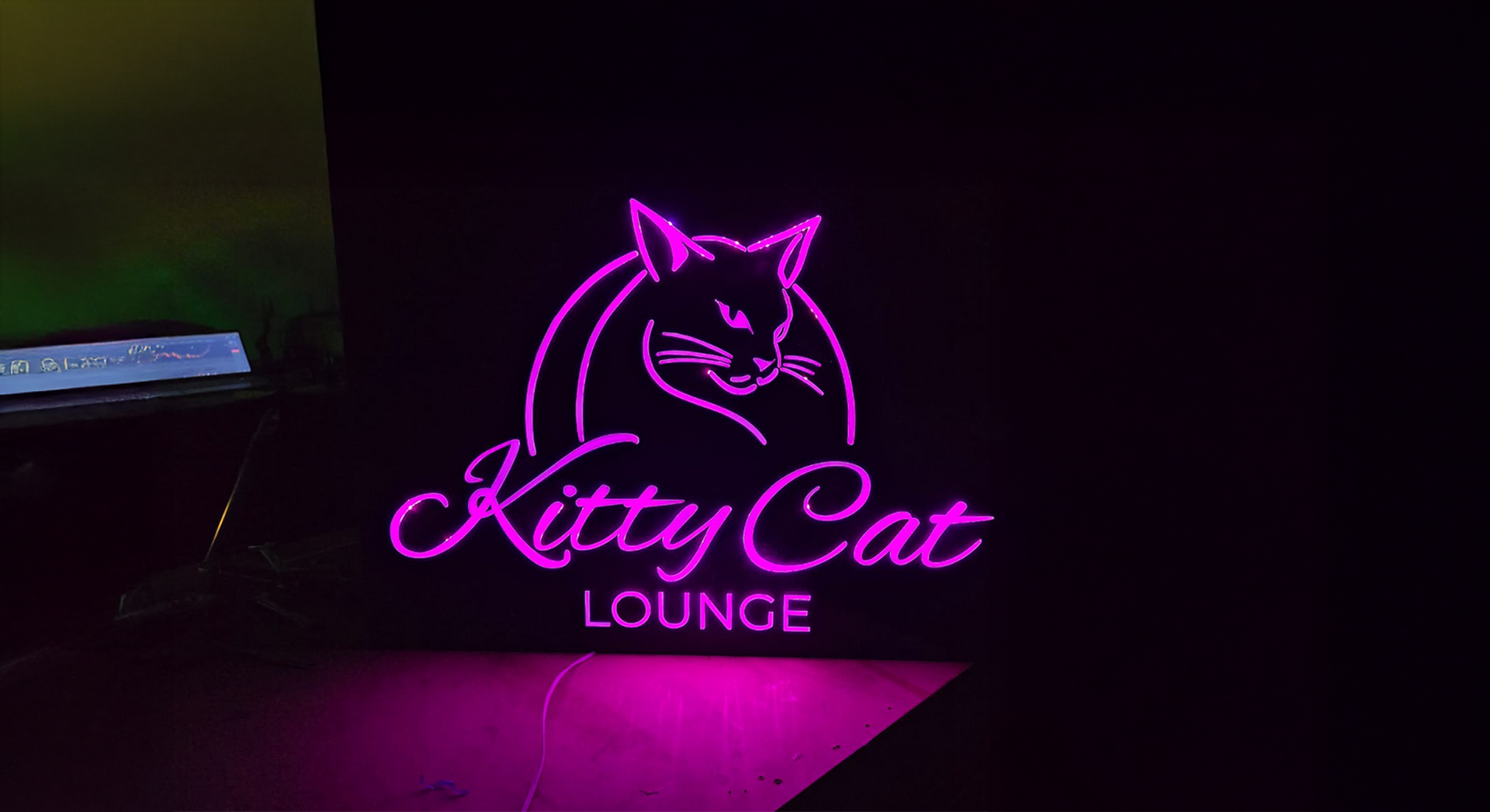Neon sign for Kitty Cat Lounge: pink cat silhouette, cursive text, black background.