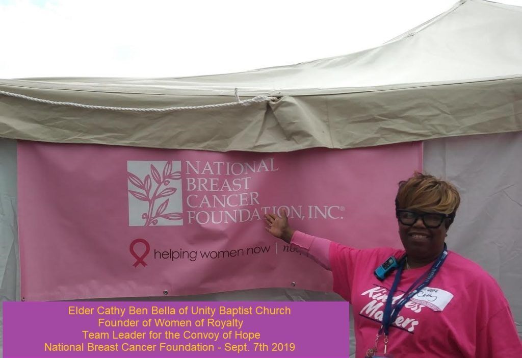 A woman in a pink shirt is standing in front of a national breast cancer foundation banner.