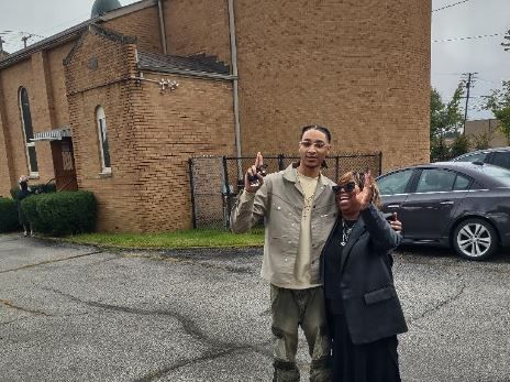 A man and a boy are standing next to each other in front of a brick building.