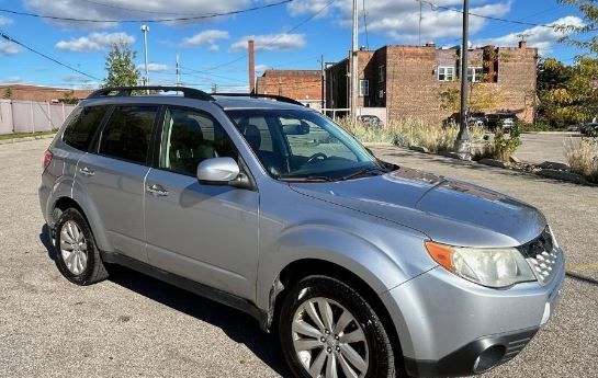 A silver subaru forester is parked in a parking lot in front of a brick building.