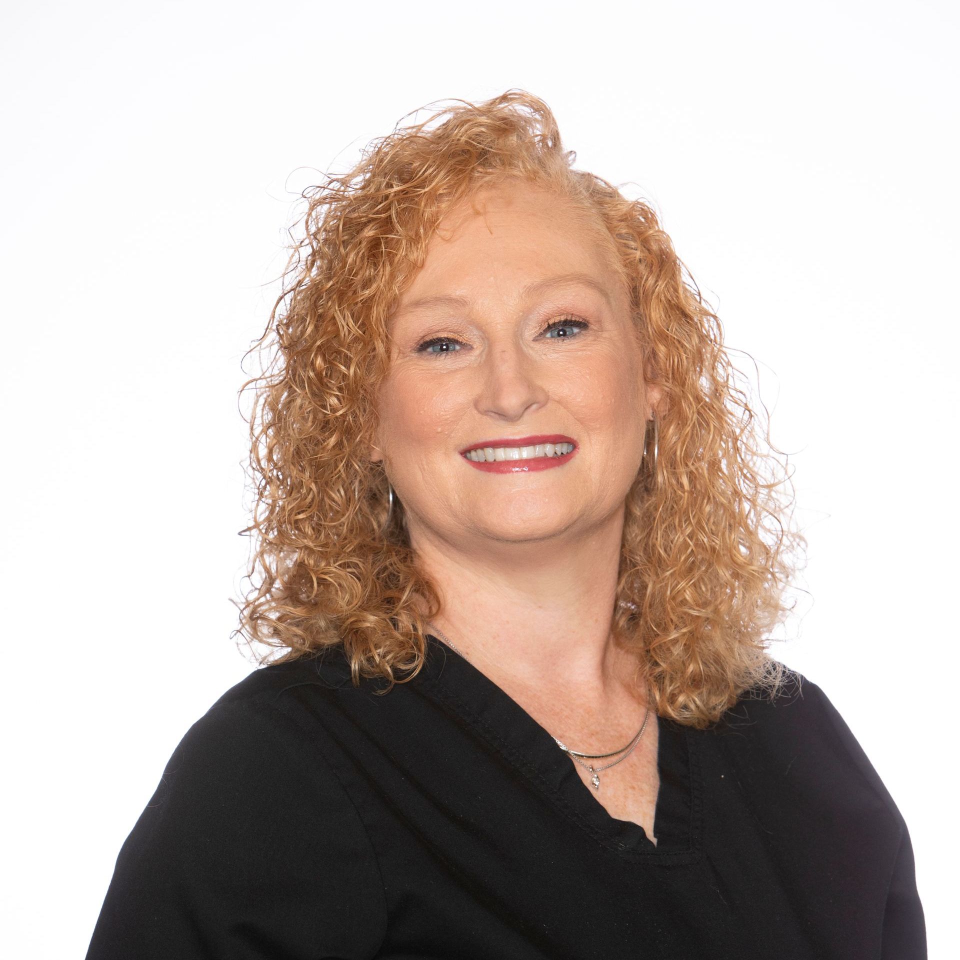 A woman with red curly hair is wearing a black shirt and smiling.