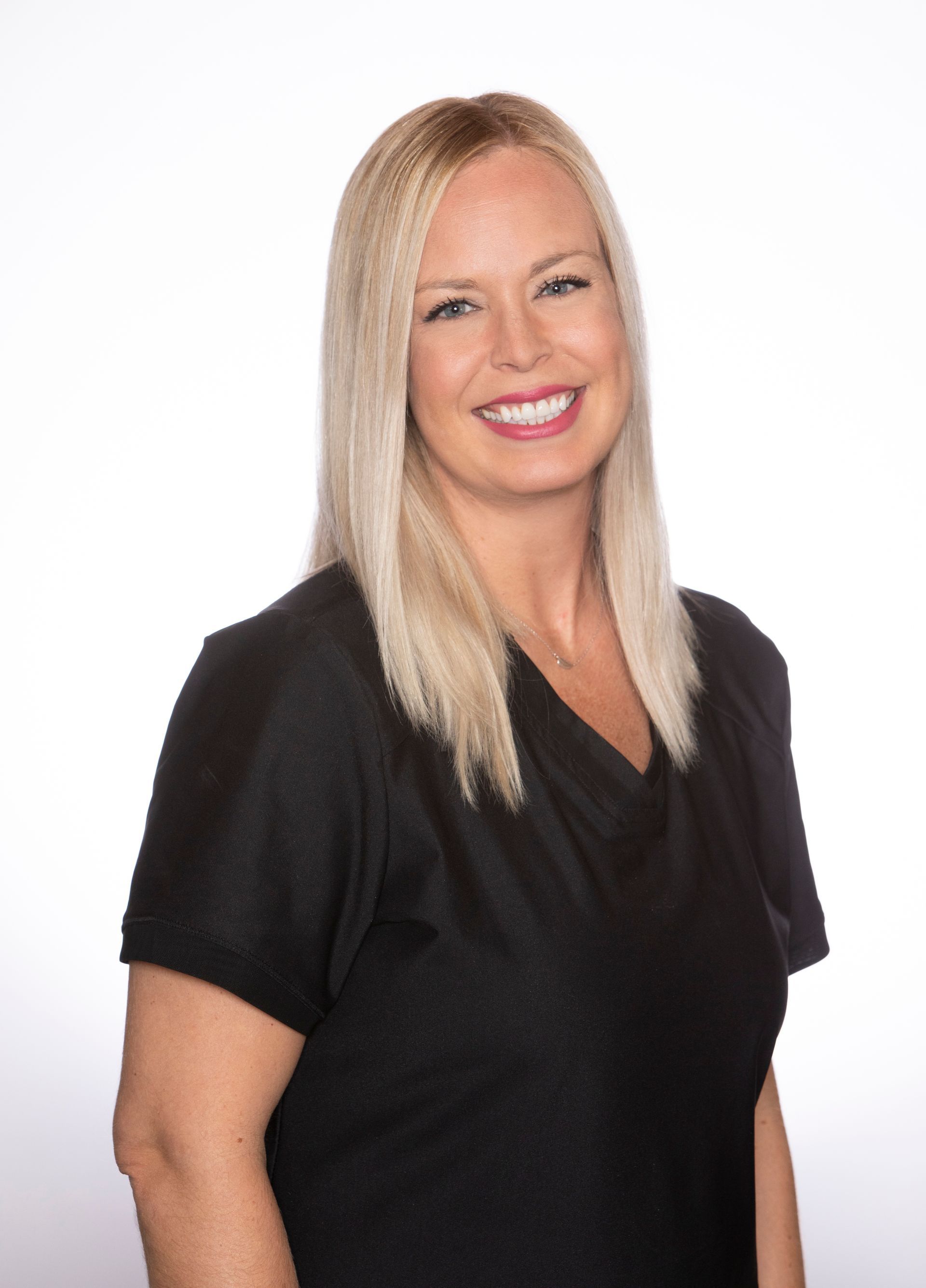 A woman in a black scrub top is smiling for the camera.