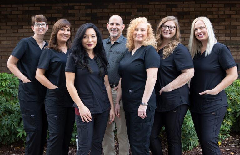 A group of people wearing black scrubs are posing for a picture.