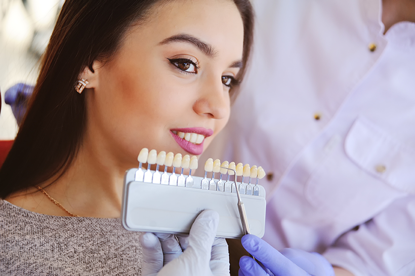 A woman is sitting in a dental chair while a dentist examines her teeth.