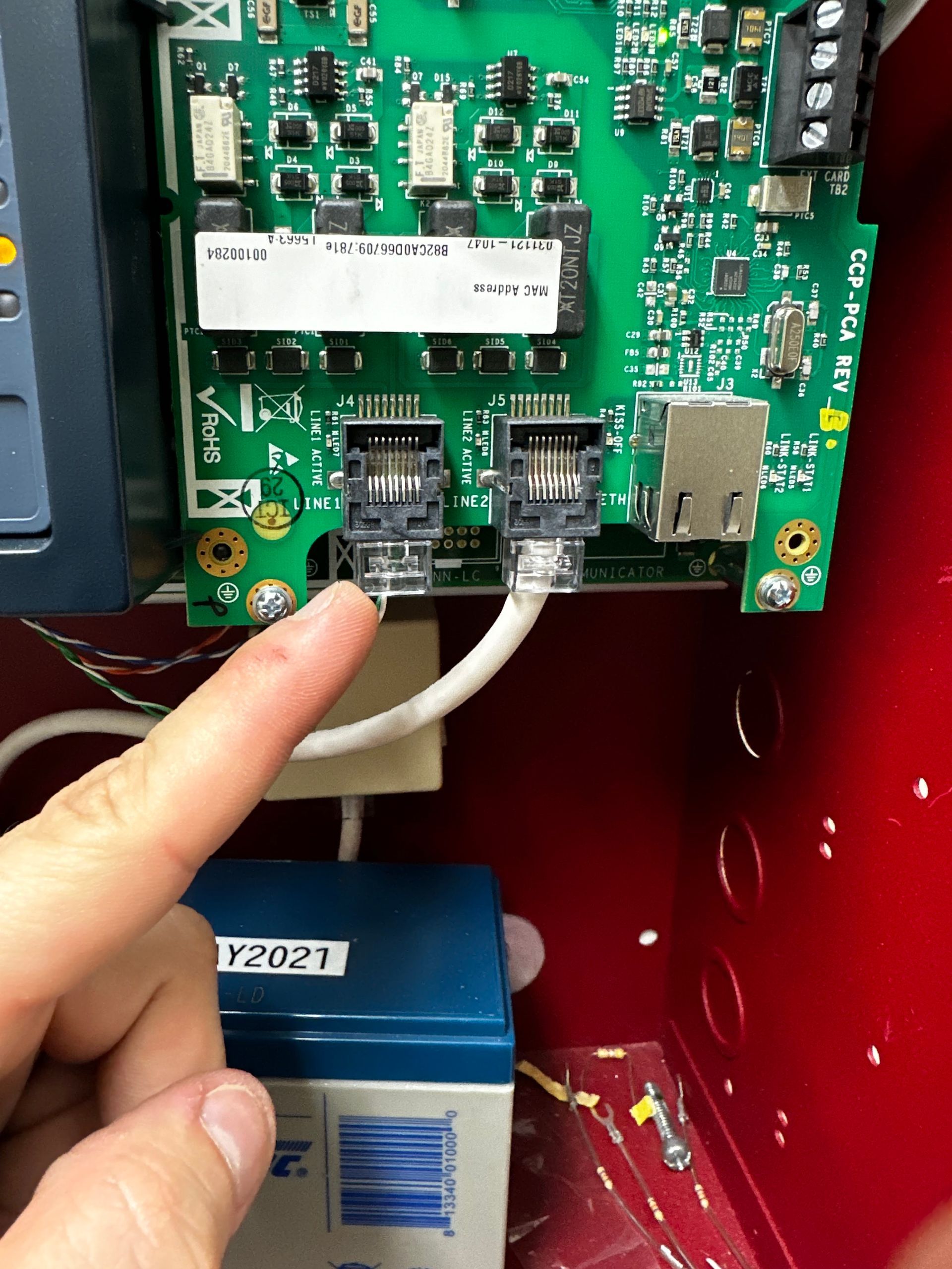 A person points at a circuit board with two ethernet ports and connected cables inside a red box.