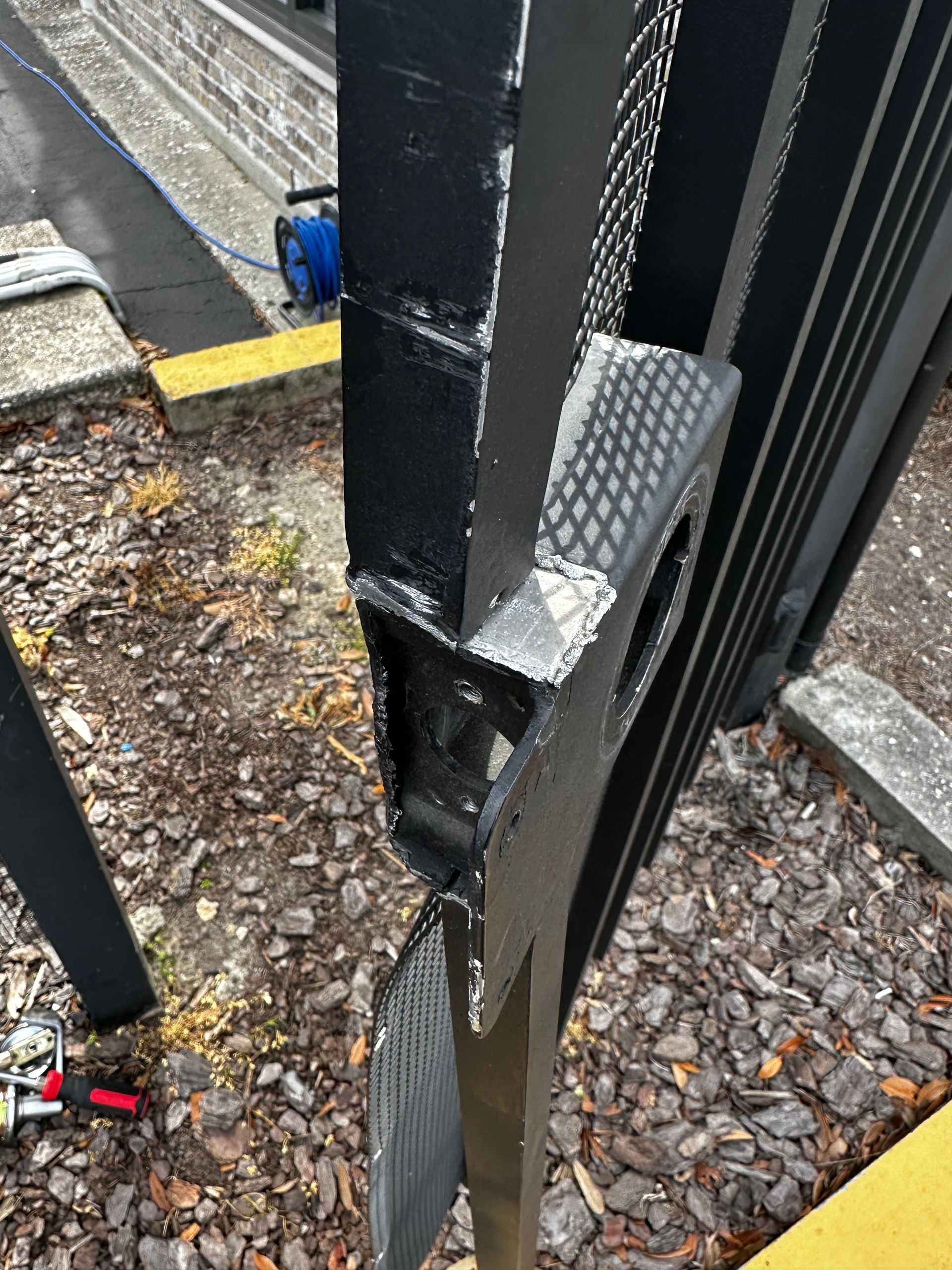 Black metal gate, broken at the joint, with a section bent out. Fresh black paint visible.