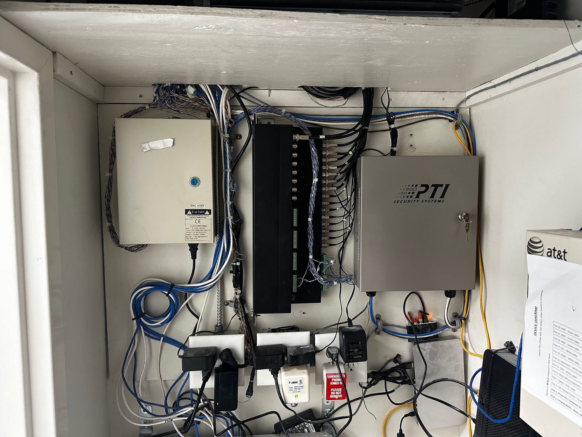 Network equipment inside a metal enclosure, with a power strip, wiring, and PTI labeled box.