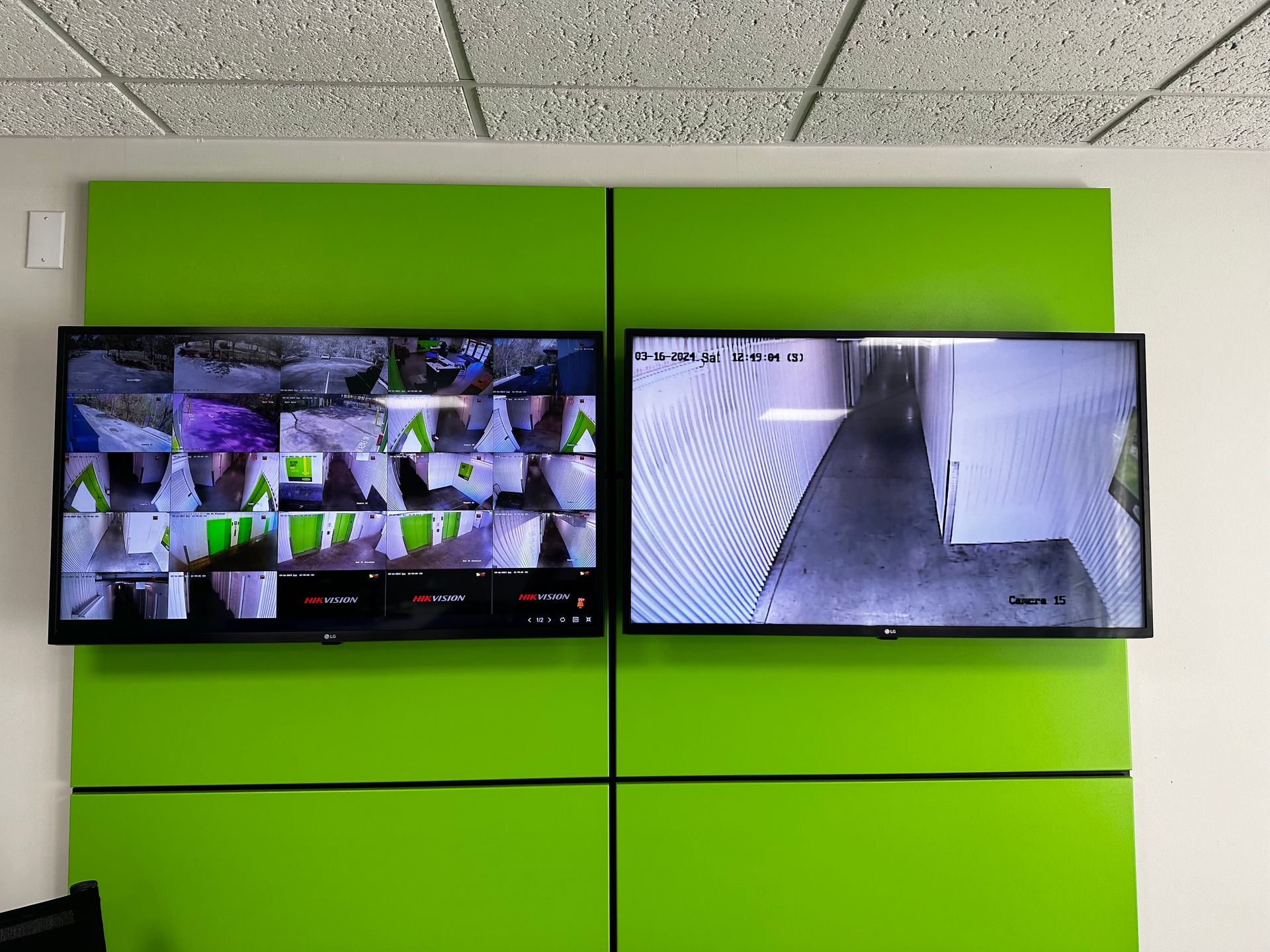 Two monitors displaying security camera feeds, mounted on green wall panels.