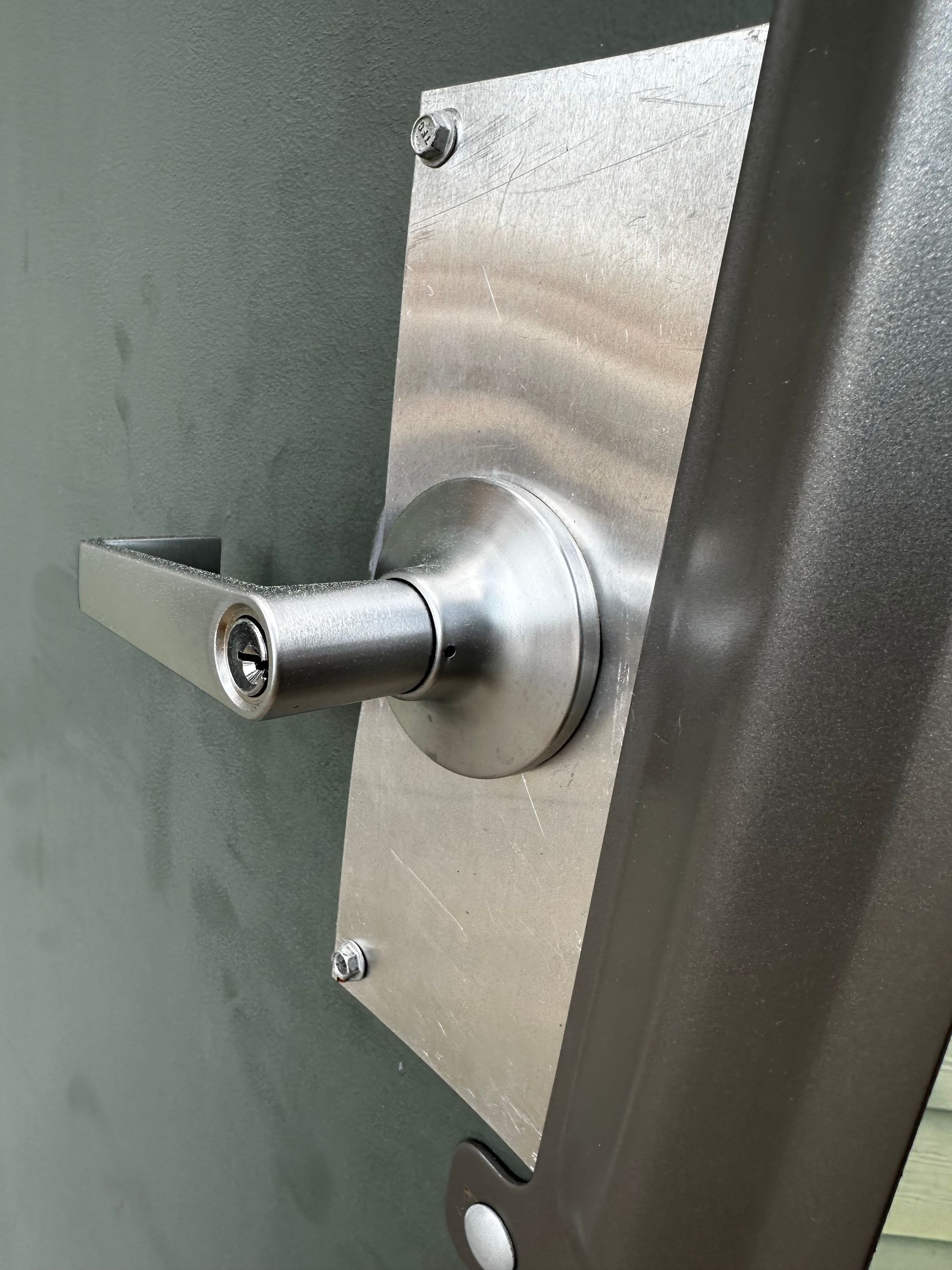 Metal door lever with keyhole on a gray door.