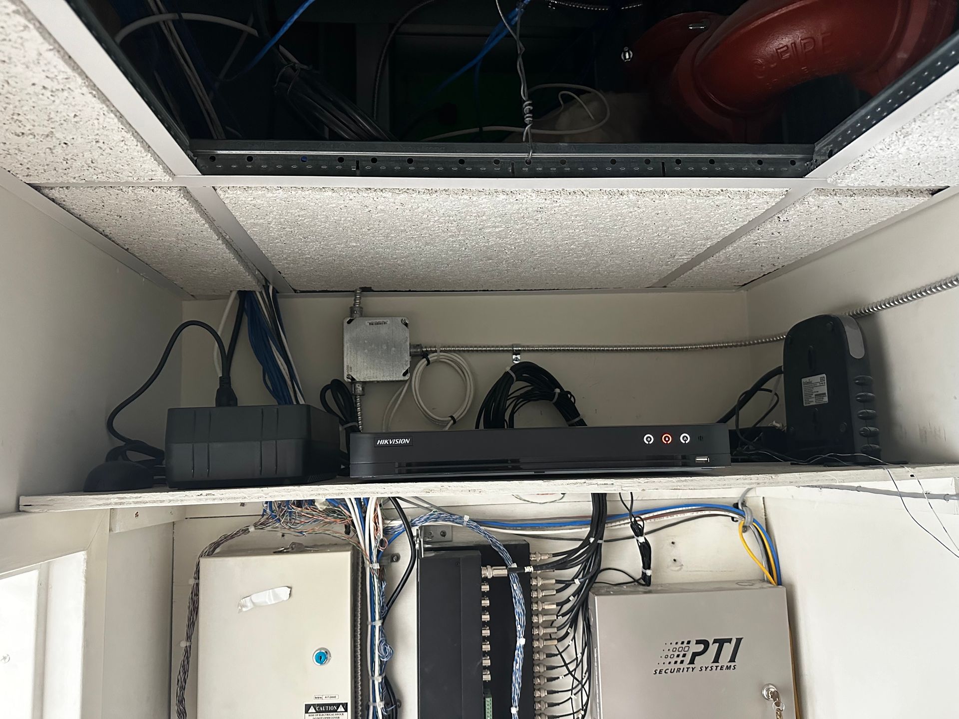 Ceiling cabinet with network equipment: DVR, router, cables, above other electronics.