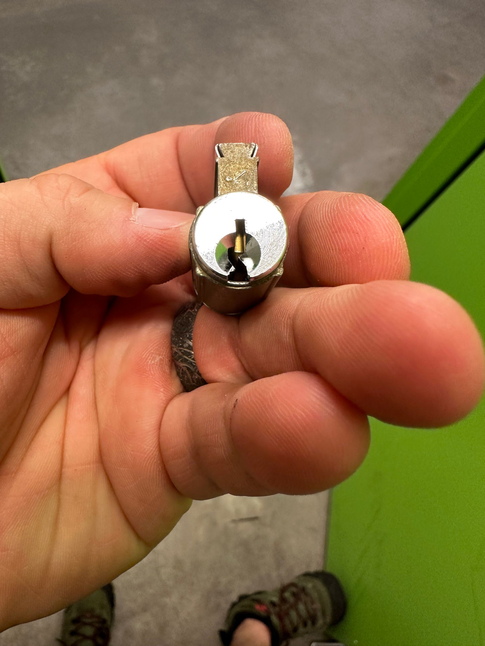 Close-up of a silver cylinder lock held in a hand, angled slightly toward the camera. A keyhole is visible.