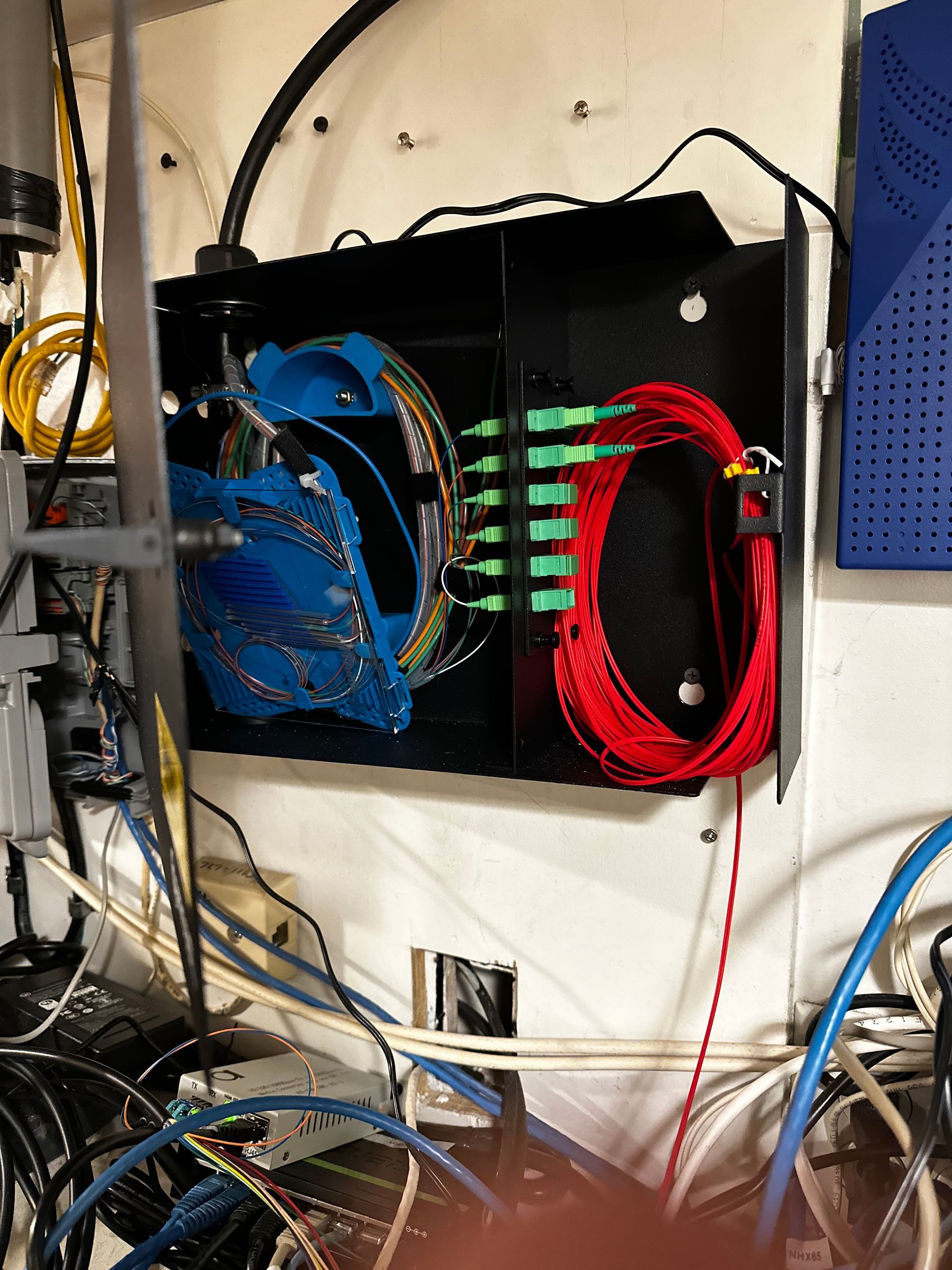 Black fiber optic enclosure with blue and red cables, green connectors, and a tangle of other cables.
