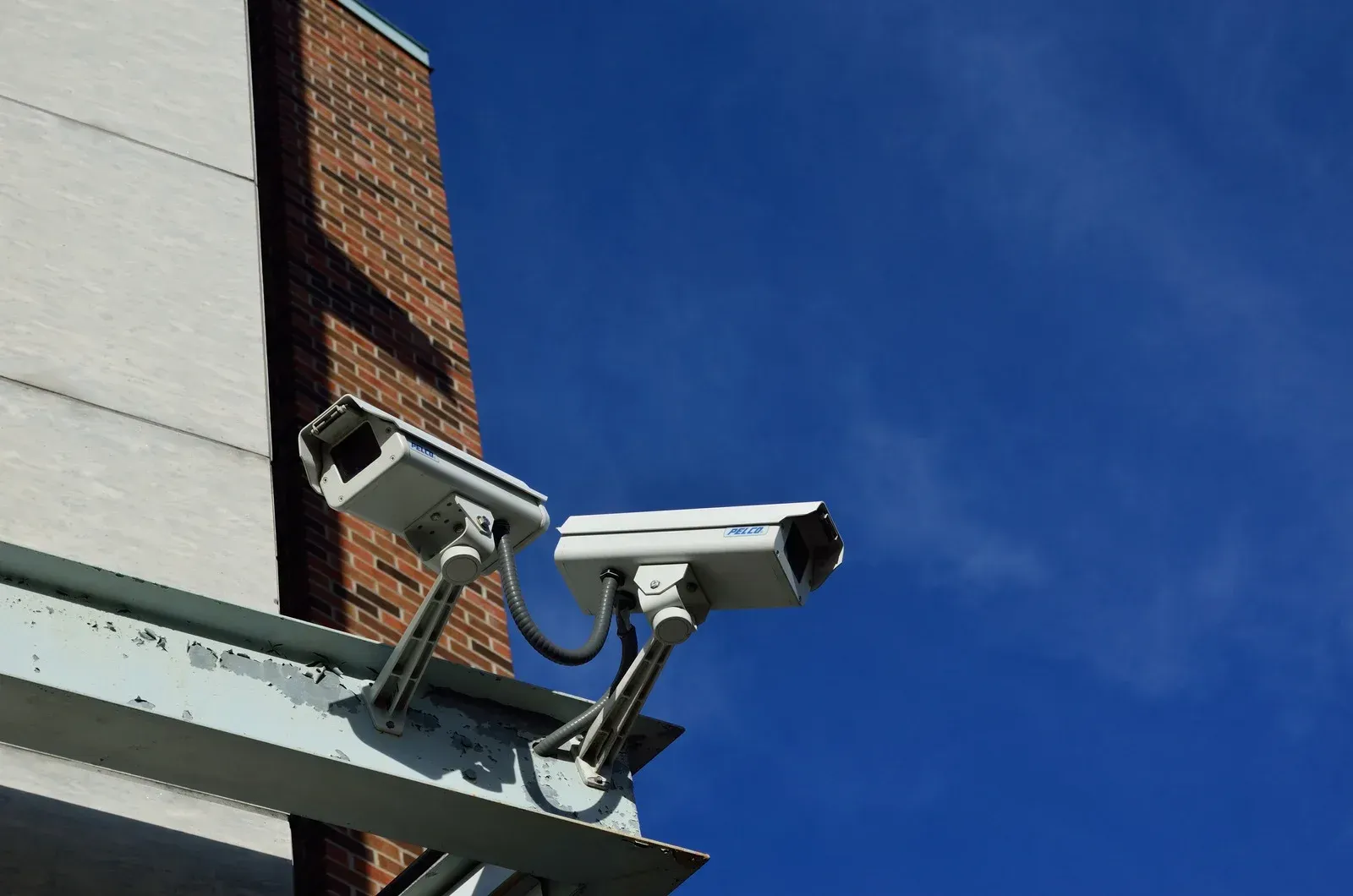 Two security cameras mounted on a building, angled against a blue sky.