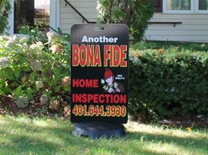 A lawn sign in front of a house with bushes reads