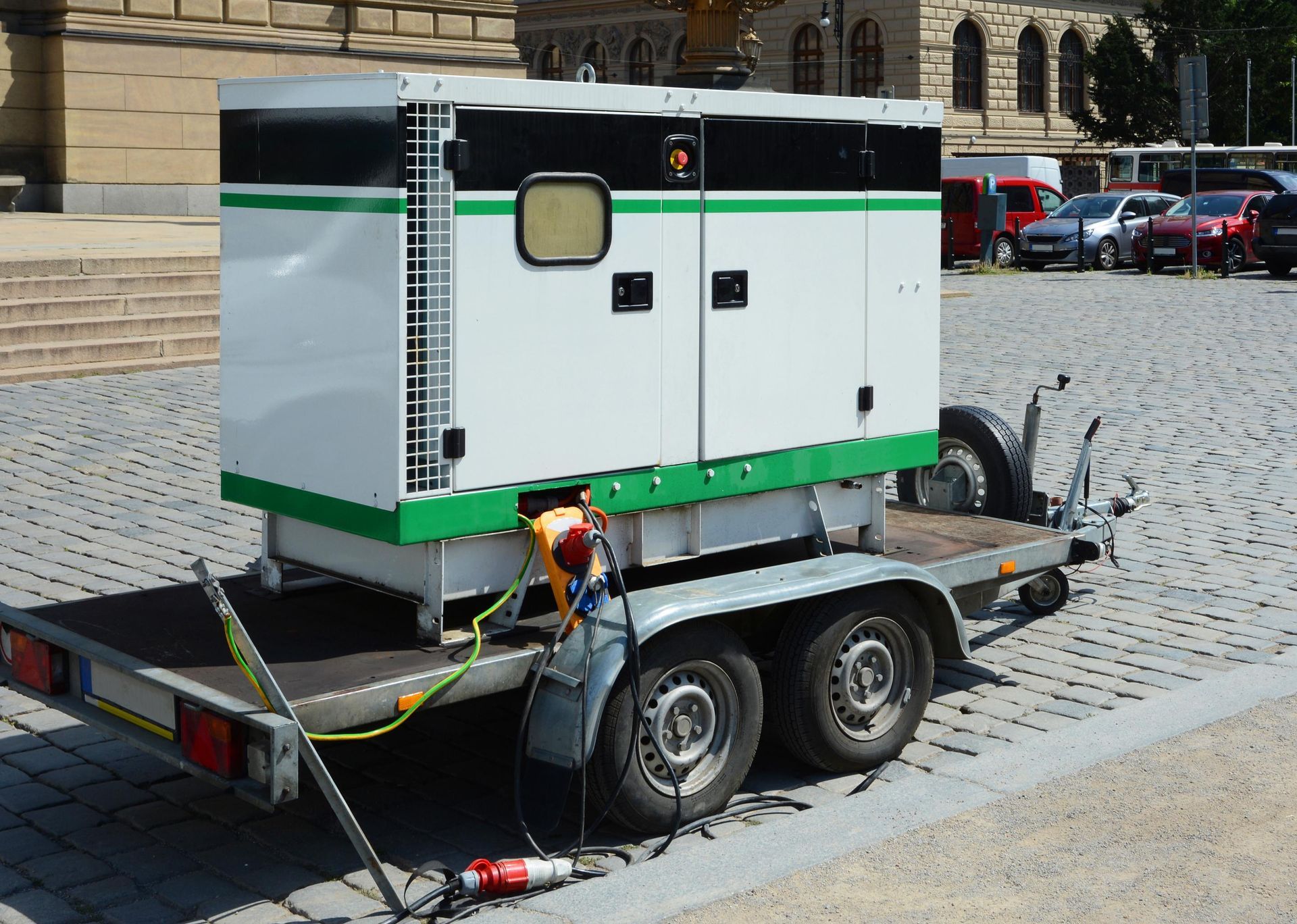 Generator on a trailer, white with green trim, parked on cobblestones.