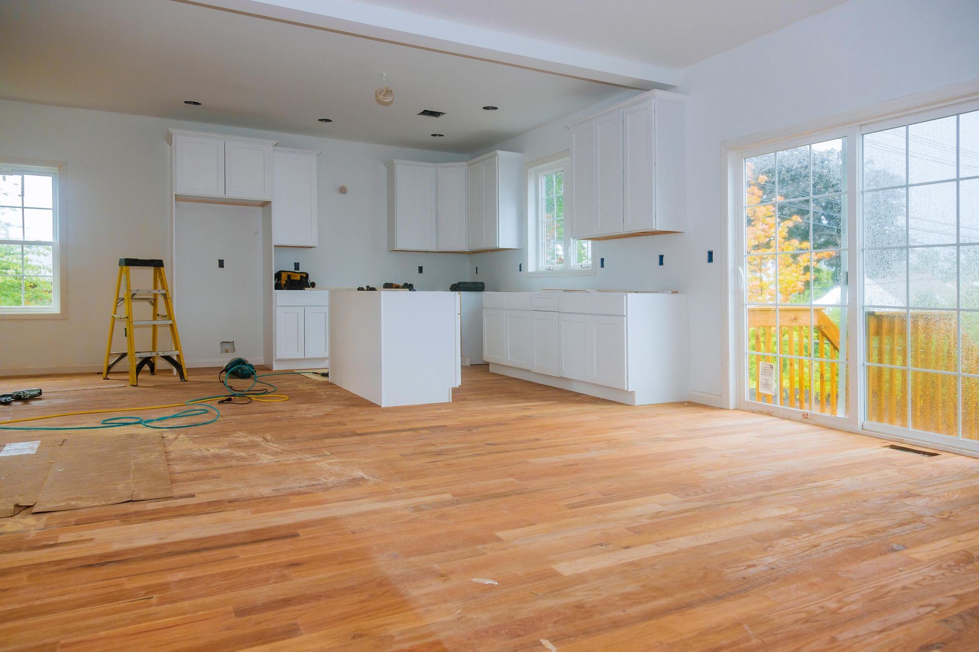 Kitchen renovation: White cabinets, wooden floor, unfinished. Yellow ladder, sliding glass door.