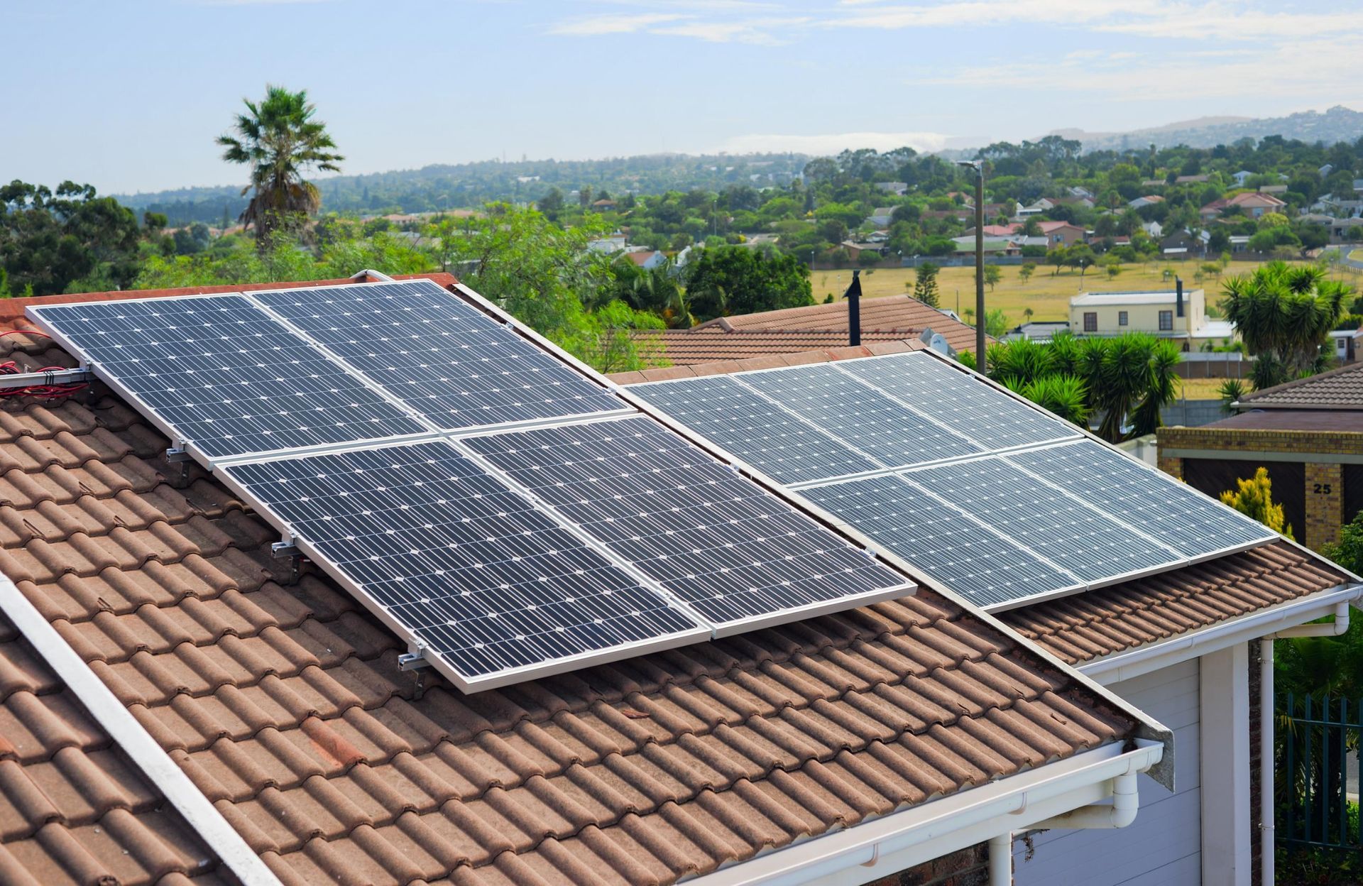 Solar panels installed on a residential tile roof, with a suburban landscape in the background.