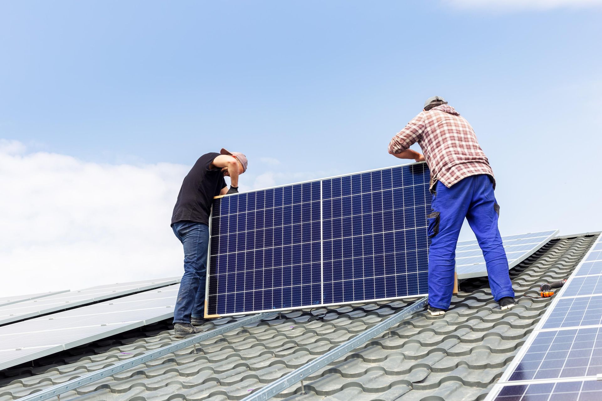 Two workers installing a solar panel on a rooftop against a blue sky.