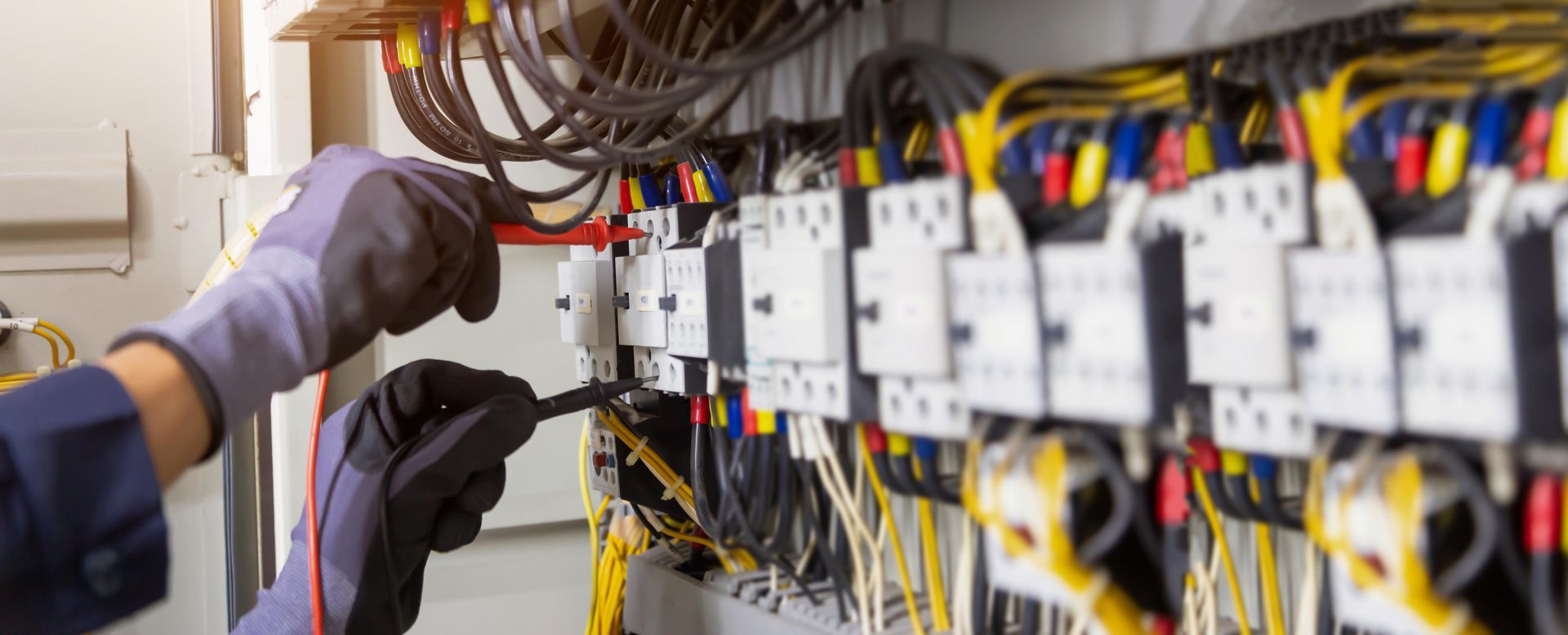 Electrician wearing gloves working on electrical wiring in a panel, using a tool.