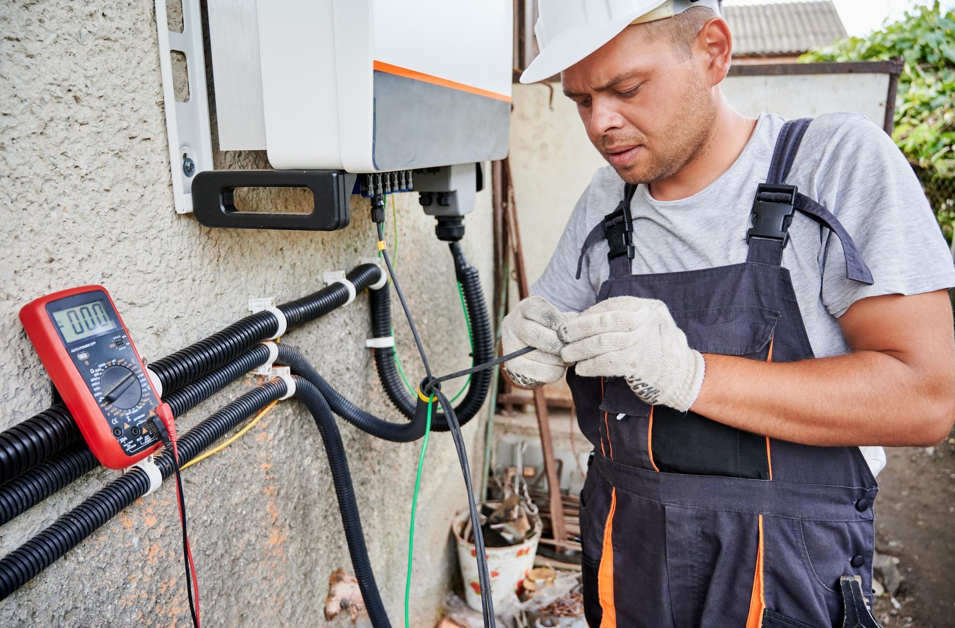 Electrician working on electrical wiring outdoors with a multimeter.