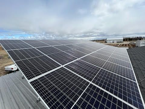 Solar panels installed on a metal roof against a cloudy sky.