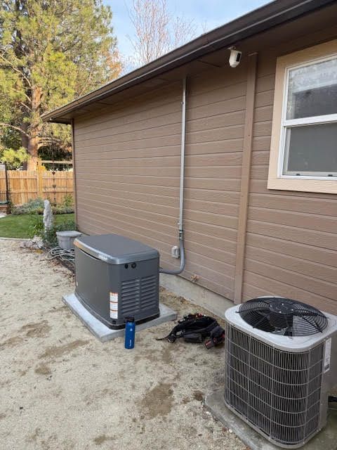 A generator and air conditioning unit sit outside a tan building. A security camera is mounted above.