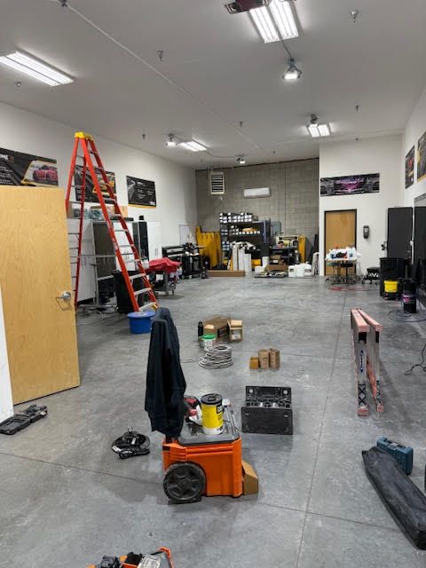 Spacious garage with tools and equipment scattered on the concrete floor. A red ladder leans against the wall.