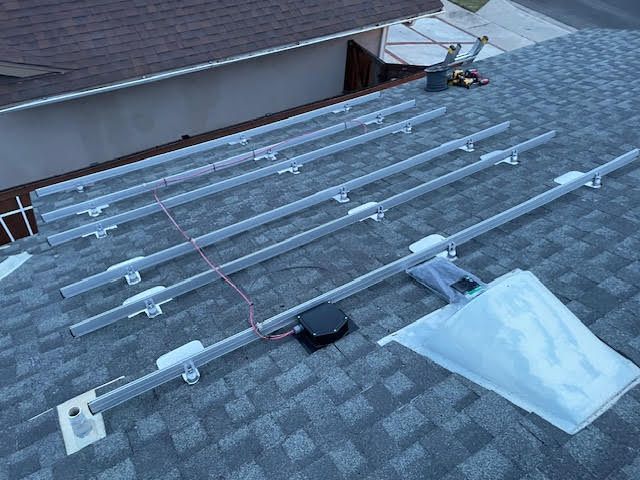 Solar panel mounting rails and components laid out on a shingled roof, ready for installation.