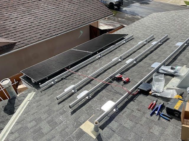 Solar panel installation on a rooftop with panels, rails, tools, and a dark shingled roof.