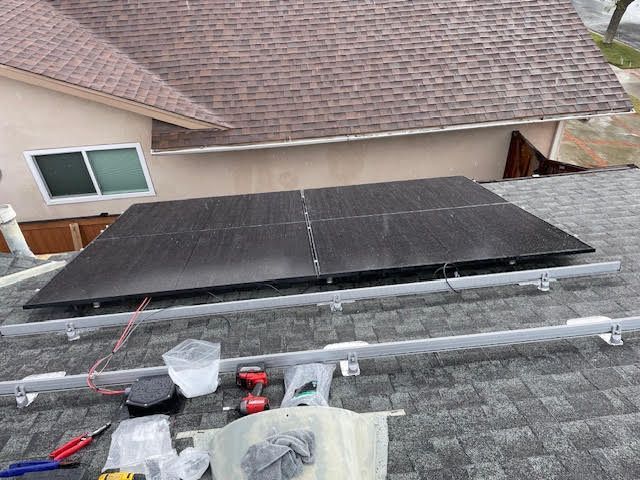 Solar panels installed on a brown shingled roof with mounting hardware and tools visible.