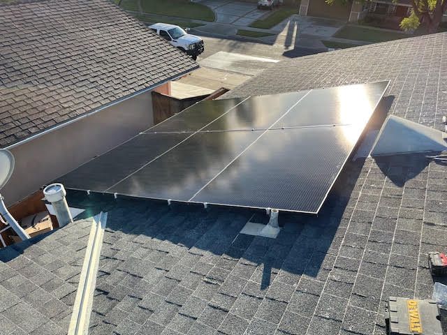 Solar panels installed on a residential roof, angled toward the sun, surrounded by shingles.