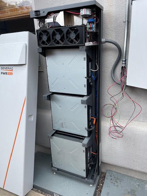 Solar battery system with three stacked battery units, cooling fans, and wiring, mounted on a wall.