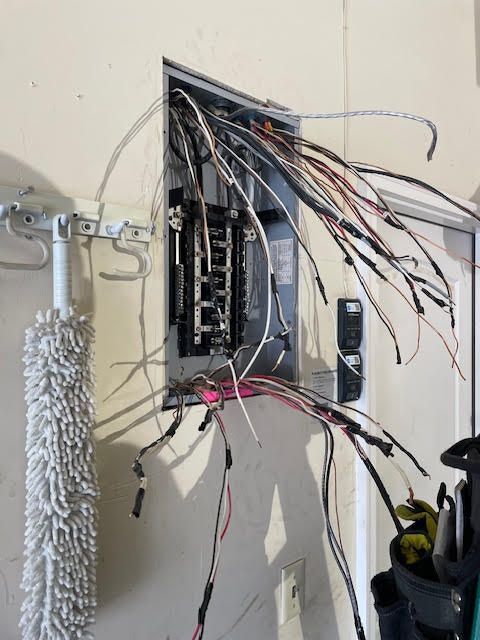 Electrical panel with exposed wires protruding from an unfinished wall opening.