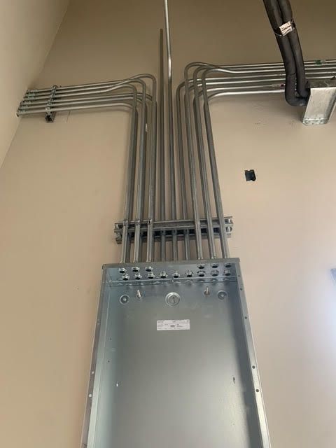 Metal electrical conduits extending from a vertical panel on a beige wall.