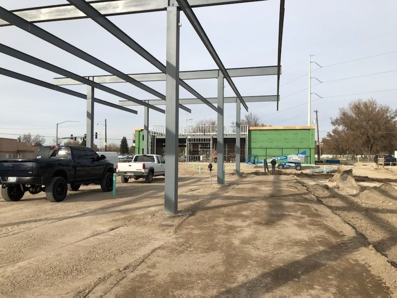 Construction site with steel framework for a structure; trucks and workers present.