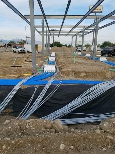 Construction site with steel framework and buried blue and white conduit.