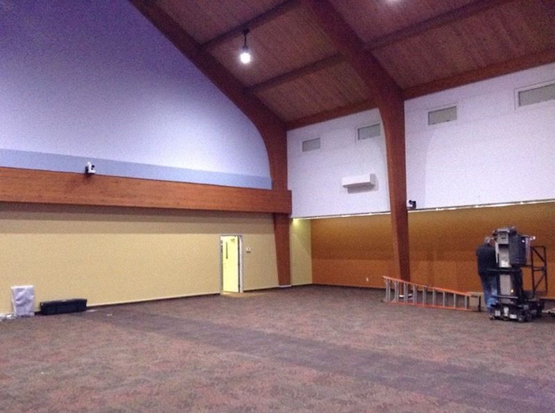 Large, empty room with brown carpet, tan walls, and a wood-beamed ceiling.