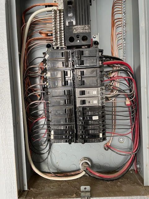 Electrical panel with numerous wires and circuit breakers.